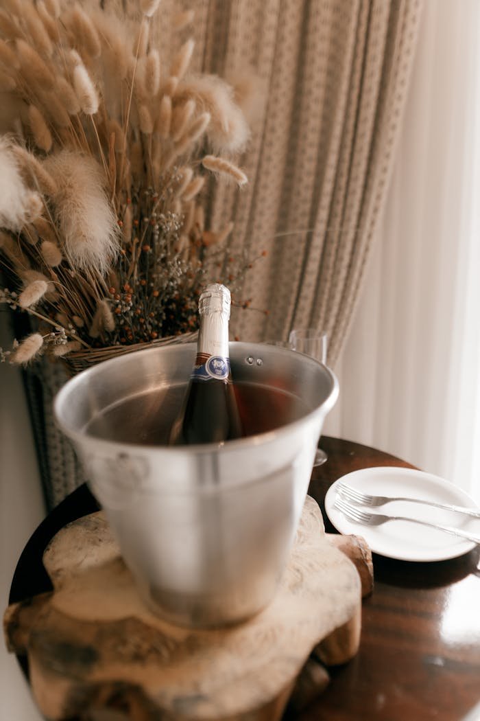 Champagne bottle in bucket surrounded by dried flowers on elegant wooden table.